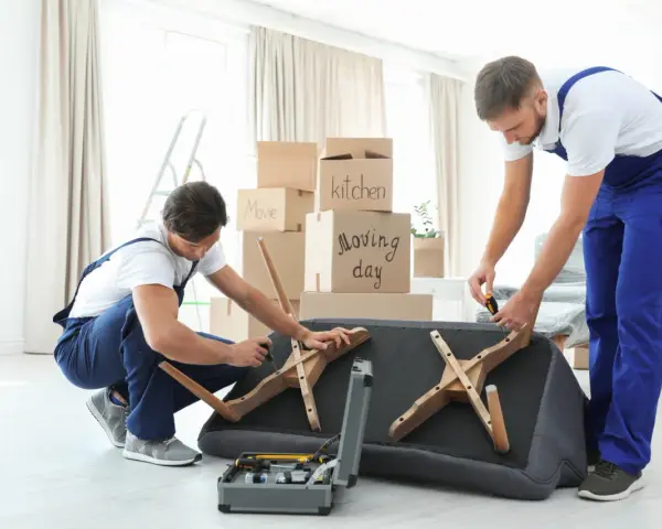 Deux déménageurs démontent un canapé fixe, outils à portée de main. Ils préparent le mobilier pour un déménagement.