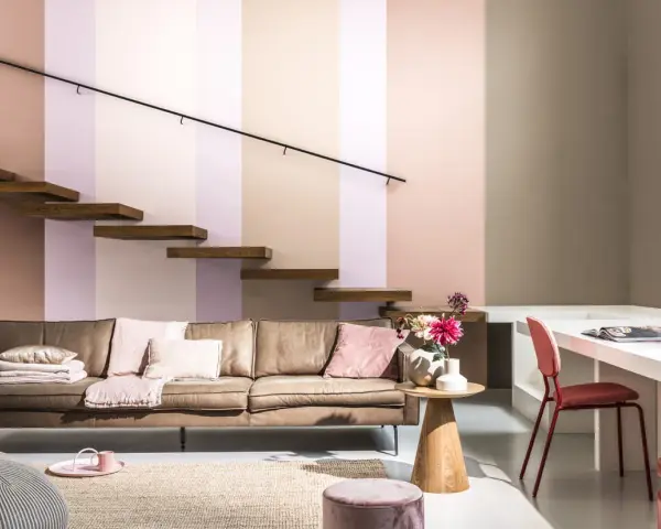Un confortable canapé en cuir marron est installé sous un escalier flottant en bois. La pièce est décorée de coussins roses et d'un tapis en jute.