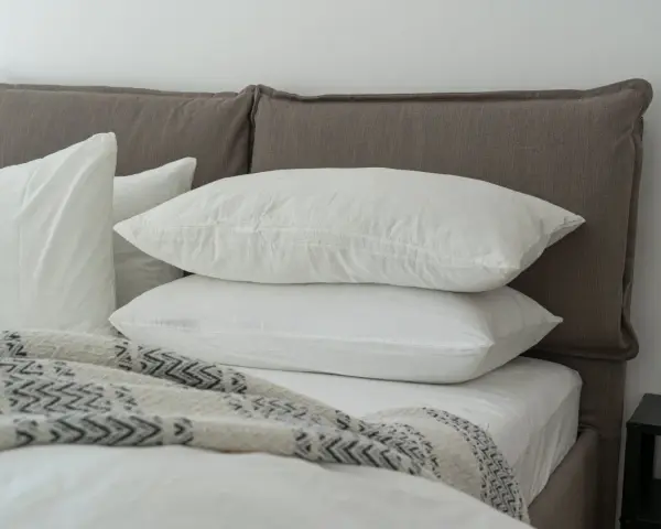 Lit douillet avec deux oreillers blancs empilés, une couverture à motifs et un drap housse ou protège matelas immaculé.