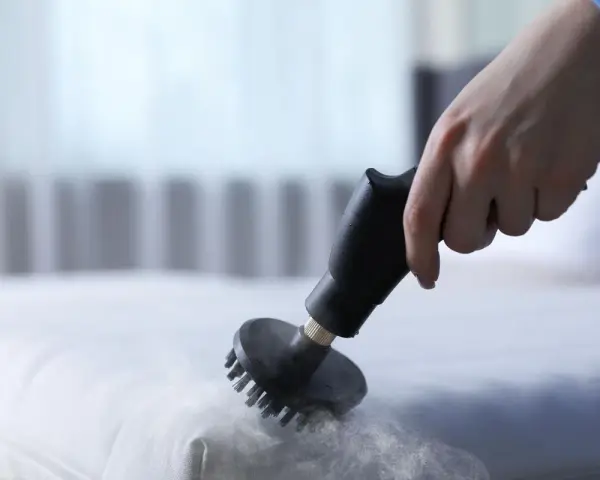 Main d'une personne utilisant un nettoyeur vapeur pour nettoyer un matelas en mousse. Une méthode efficace pour savoir comment nettoyer un matelas en mousse.