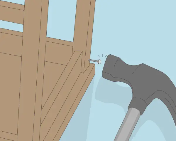 Un marteau s'apprête à frapper un clou dans la structure en bois d'un fauteuil qui grince.