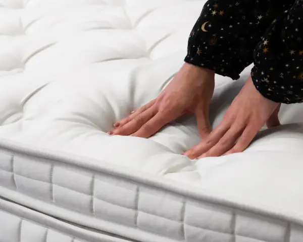 Mains testant la douceur d'un matelas blanc matelassé. Quel matelas pour mal de dos dur ou mou ? Le confort est essentiel.