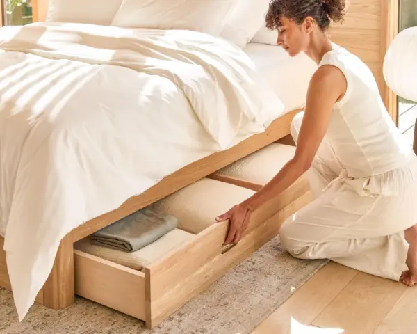 Une femme range des draps dans un tiroir de lit en bois.