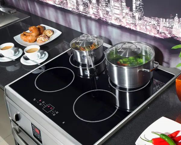 Plaque à induction moderne avec deux casseroles en marche, symbolisant la puissance et l'efficacité. Deux tasses de café et des viennoiseries sont prêtes pour le petit-déjeuner.