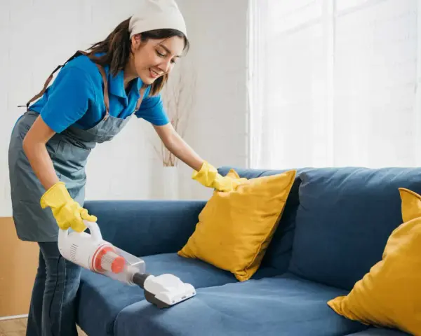 Femme nettoyant un canapé bleu avec un aspirateur pour éliminer la mauvaise odeur du tissu.