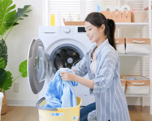 Une femme charge du linge bleu dans une machine à laver. Le cycle de rincage de la machine à laver est terminé.