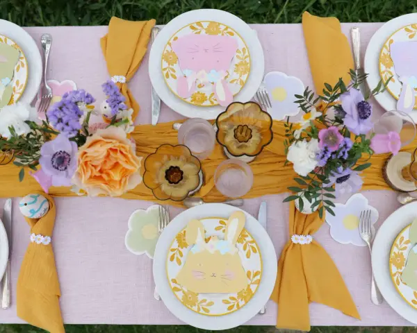 Jolie table de Pâques avec des lapins en papier, des fleurs fraîches et des œufs décorés. Une belle idée déco table Pâques pour un repas printanier.