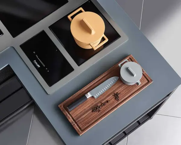 Cuisine moderne avec plaque de cuisson intégrée. Un couteau de chef et des épices sur une planche à découper en bois. Une casserole jaune sur la plaque.