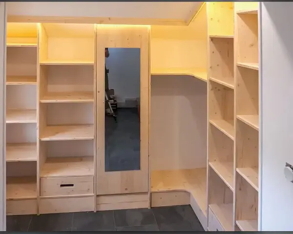 Construction d'une armoire sur mesure avec des portes coulissantes et des étagères en bois clair. Un miroir est intégré.