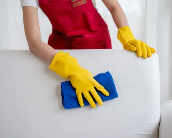 Mains gantées de jaune nettoient un canapé en cuir blanc, redonnant son éclat à ce meuble autrefois très sale.