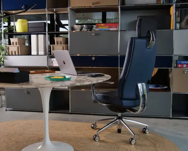 Un fauteuil de bureau design bleu marine, un bureau rond en marbre et un ordinateur portable créent un espace de travail élégant.
