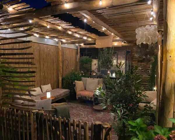 Une terrasse de jardin aménagée en coin cocooning, avec des banquettes confortables, des lumières douces et une ambiance chaleureuse.