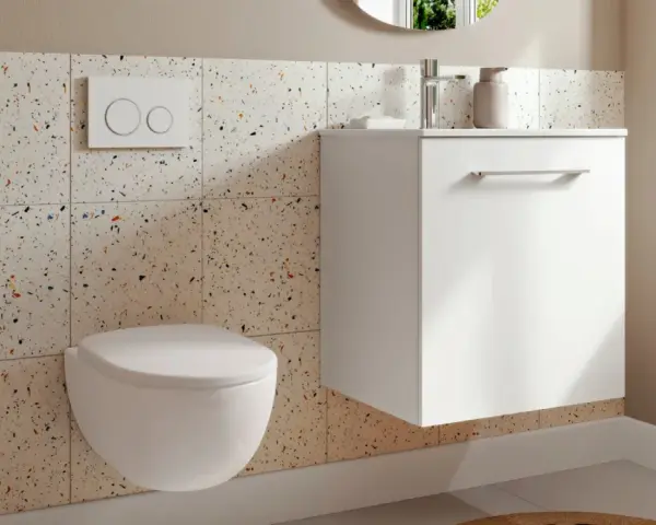 Une petite toilette moderne suspendue, avec un mur en carreaux de terrazzo colorés et un meuble blanc flottant.