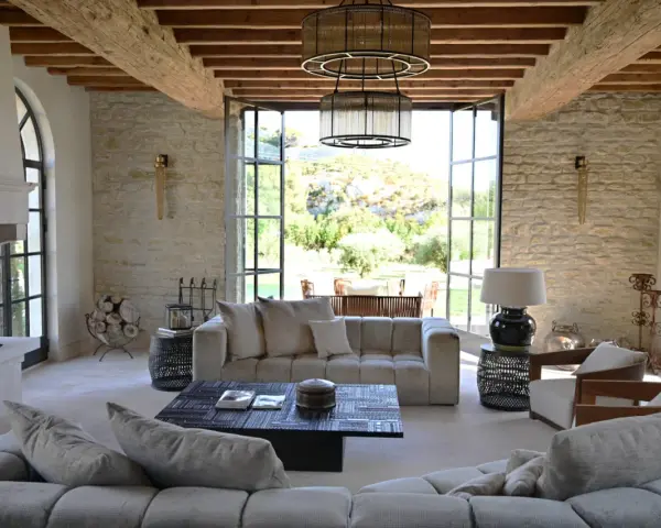 L'intérieur d'un mas provençal baigné de lumière, avec des poutres apparentes, des murs en pierre et une vue imprenable sur la campagne.