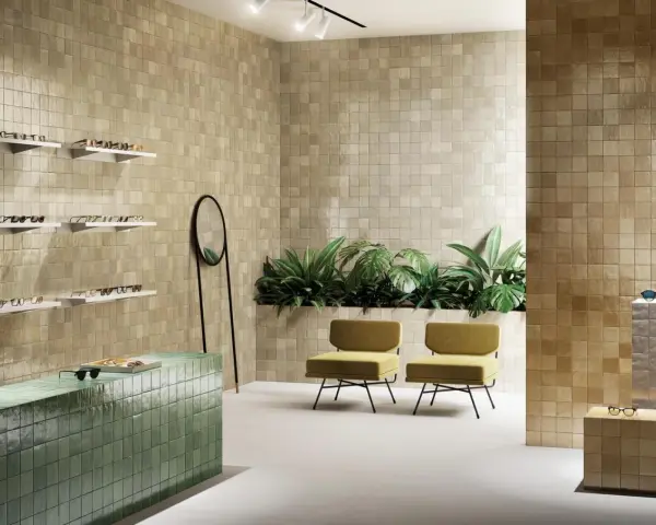 Un espace moderne avec des murs recouverts de **zellige** beige, un comptoir vert émeraude, des plantes luxuriantes et des chaises jaunes.