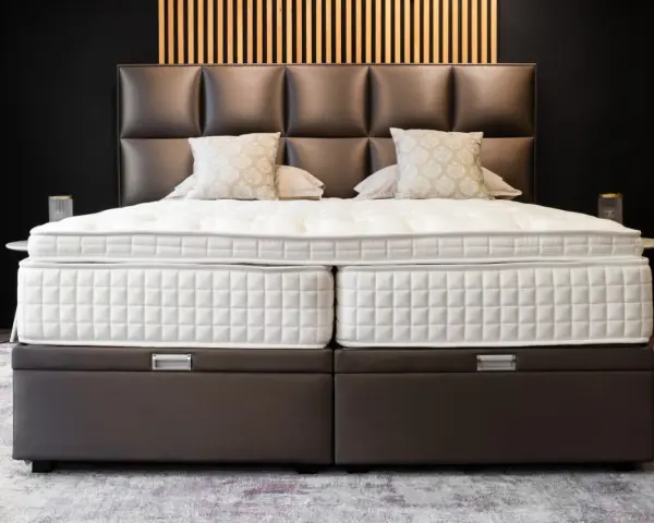 Lit, deux matelas blancs sur des sommiers marron. Le matelas trop grand pour sommier crée un léger débord.