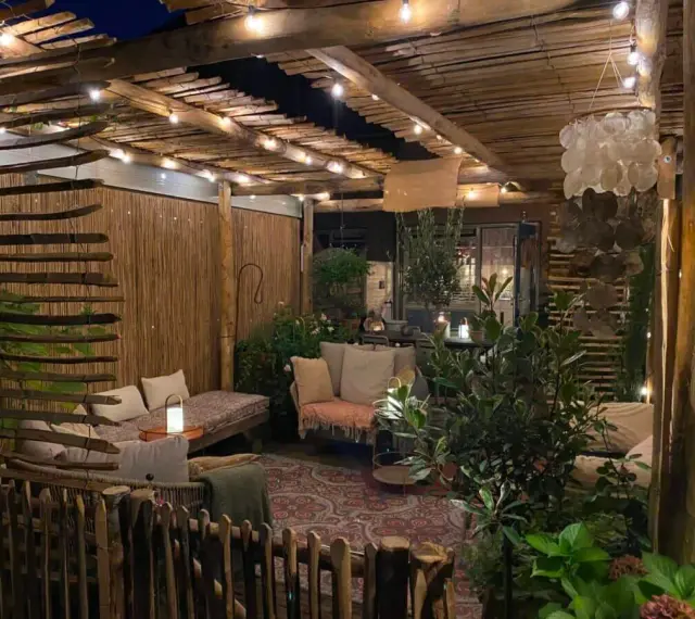 Une terrasse de jardin aménagée en coin cocooning, avec des banquettes confortables, des lumières douces et une ambiance chaleureuse.