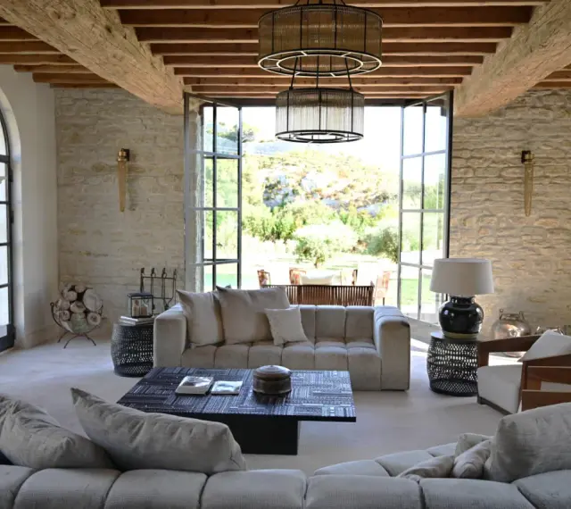 L'intérieur d'un mas provençal baigné de lumière, avec des poutres apparentes, des murs en pierre et une vue imprenable sur la campagne.