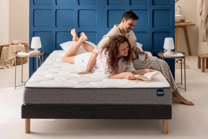 Un couple profite d'un moment de détente sur un matelas de taille lit 2 places. L'homme lit, la femme lit un livre.