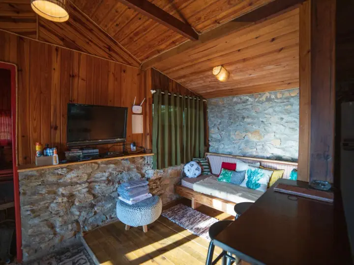 Un salon cosy en bois et pierre, avec canapé, TV et table. Idéal pour savoir comment agrandir une pièce avec style.
