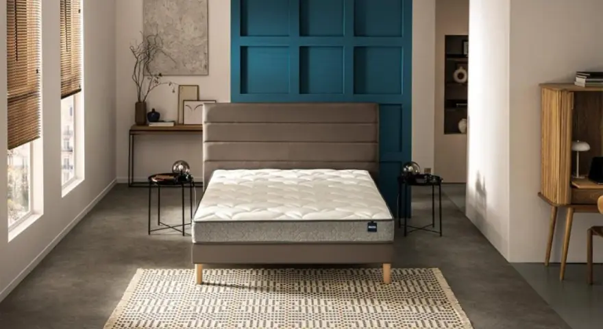 Un lit moderne avec un matelas blanc et un sommier gris, sur un tapis géométrique. Le prix moyen d'un bon matelas est un investissement pour le confort.