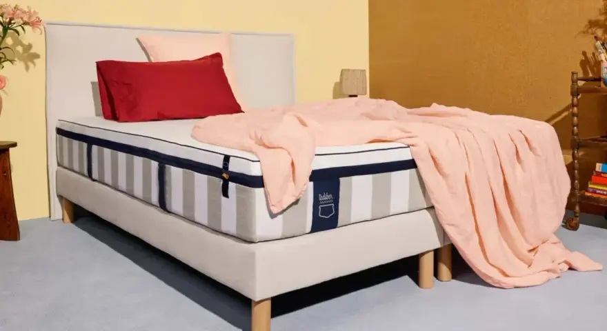 Un matelas rayé, drapé d'une couverture rose pâle, avec des coussins rouge et rose. La question est : combien de ressorts pour un bon matelas ?