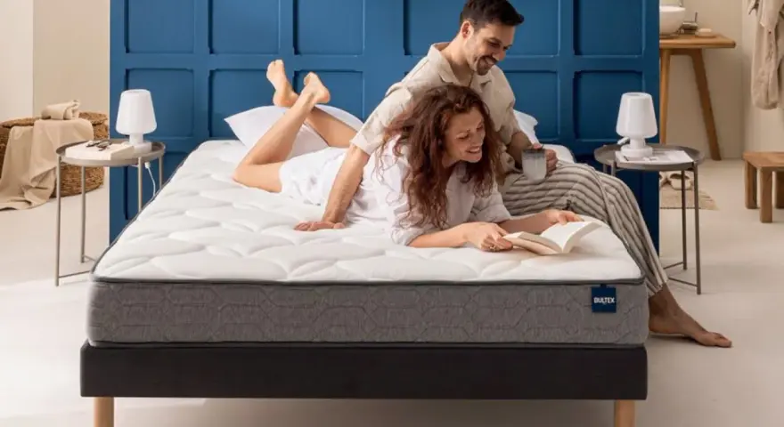 Un couple profite d'un moment de détente sur un matelas de taille lit 2 places. L'homme lit, la femme lit un livre.