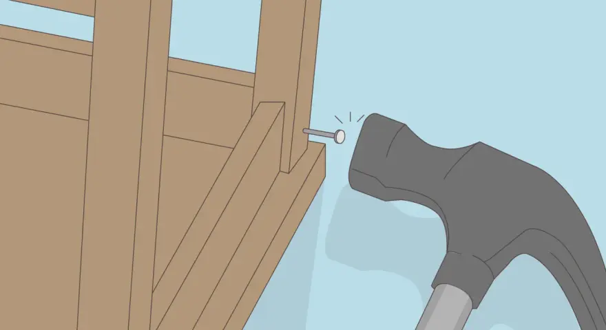 Un marteau s'apprête à frapper un clou dans la structure en bois d'un fauteuil qui grince.