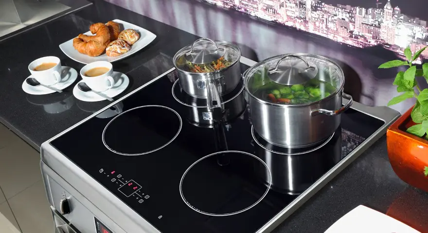 Plaque à induction moderne avec deux casseroles en marche, symbolisant la puissance et l'efficacité. Deux tasses de café et des viennoiseries sont prêtes pour le petit-déjeuner.