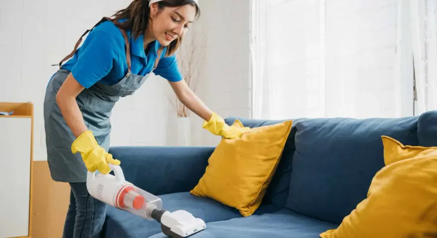 Femme nettoyant un canapé bleu avec un aspirateur pour éliminer la mauvaise odeur du tissu.