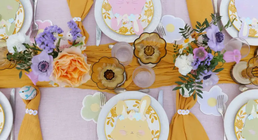 Jolie table de Pâques avec des lapins en papier, des fleurs fraîches et des œufs décorés. Une belle idée déco table Pâques pour un repas printanier.