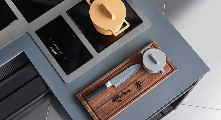 Cuisine moderne avec plaque de cuisson intégrée. Un couteau de chef et des épices sur une planche à découper en bois. Une casserole jaune sur la plaque.