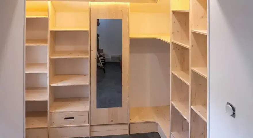 Construction d'une armoire sur mesure avec des portes coulissantes et des étagères en bois clair. Un miroir est intégré.