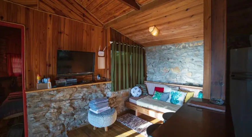 Un salon cosy en bois et pierre, avec canapé, TV et table. Idéal pour savoir comment agrandir une pièce avec style.