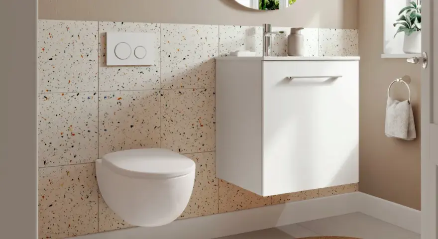 Une petite toilette moderne suspendue, avec un mur en carreaux de terrazzo colorés et un meuble blanc flottant.