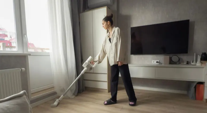 Une femme utilise un aspirateur sans fil, peut-être pour savoir quel est l'aspirateur le plus silencieux.