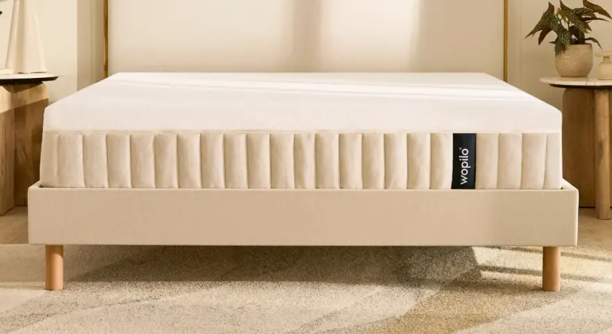 Un matelas hybride Wopilo sur un sommier beige aux pieds en bois. Quel sommier pour matelas hybride ? Ce lit offre un confort optimal.
