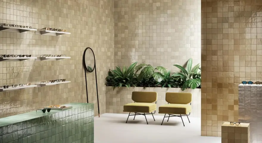 Un espace moderne avec des murs recouverts de **zellige** beige, un comptoir vert émeraude, des plantes luxuriantes et des chaises jaunes.