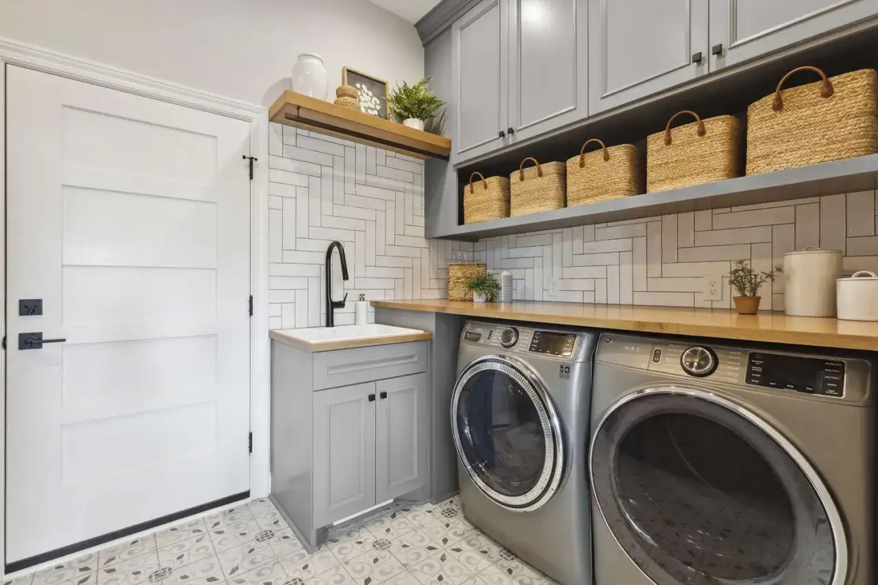 Am&eacute;nager une buanderie moderne avec lave-linge, s&egrave;che-linge, &eacute;vier gris et paniers en osier sur &eacute;tag&egrave;res.