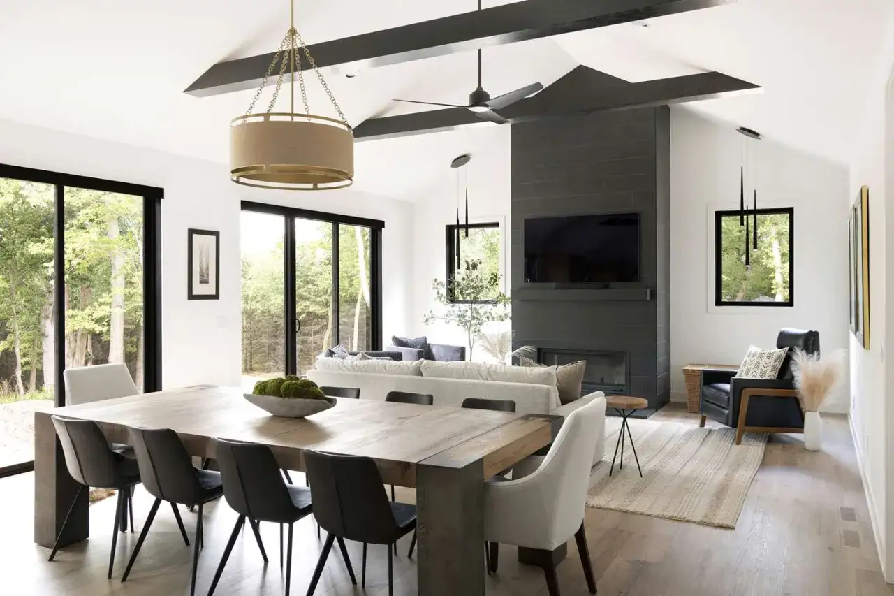 Salon moderne avec poutre apparente. Une grande table en bois domine la pièce, face à un canapé confortable et une cheminée en ardoise.
