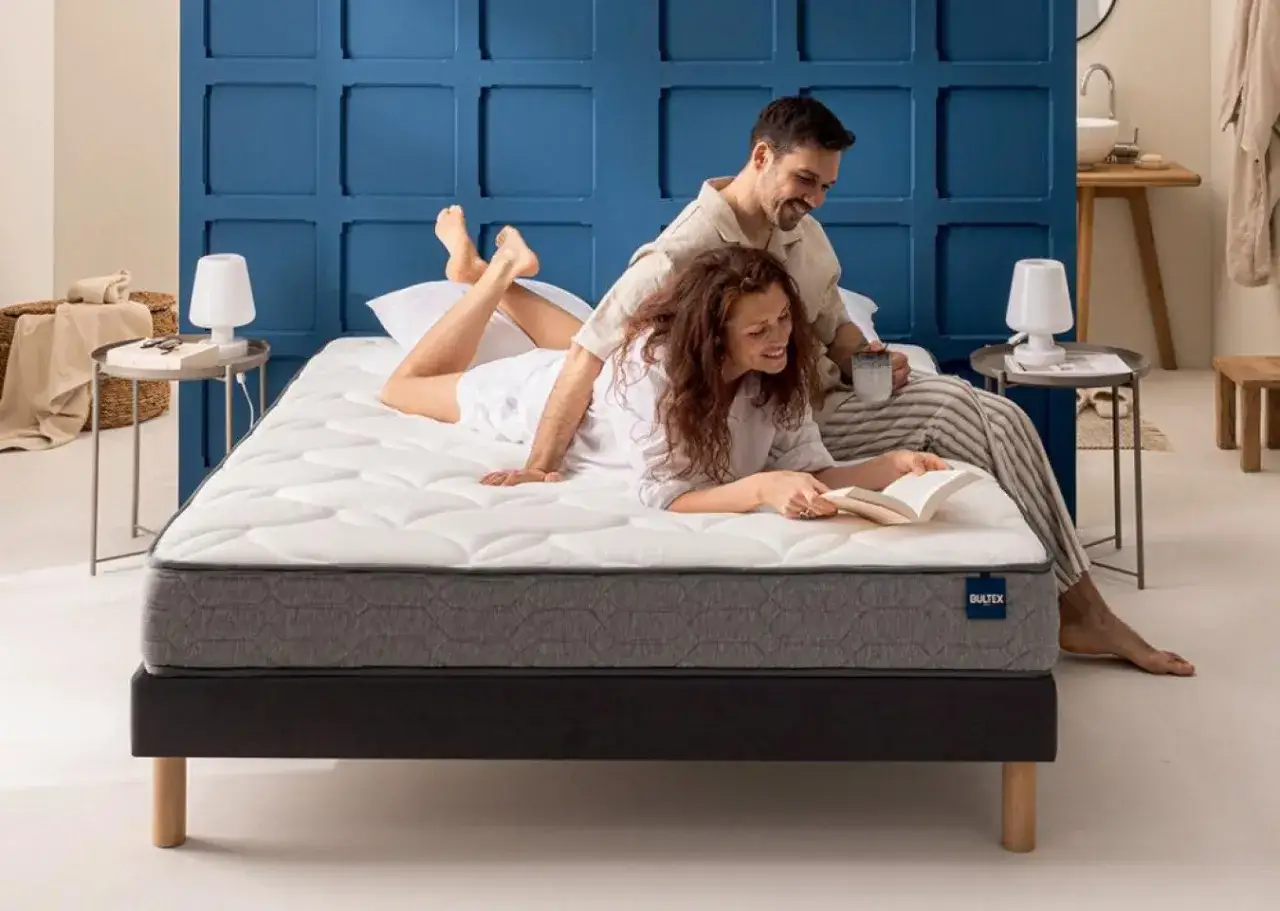 Un couple heureux profite d'un matelas confortable, parfait pour le choix literie idéal. Ils lisent et boivent un café, détendus.