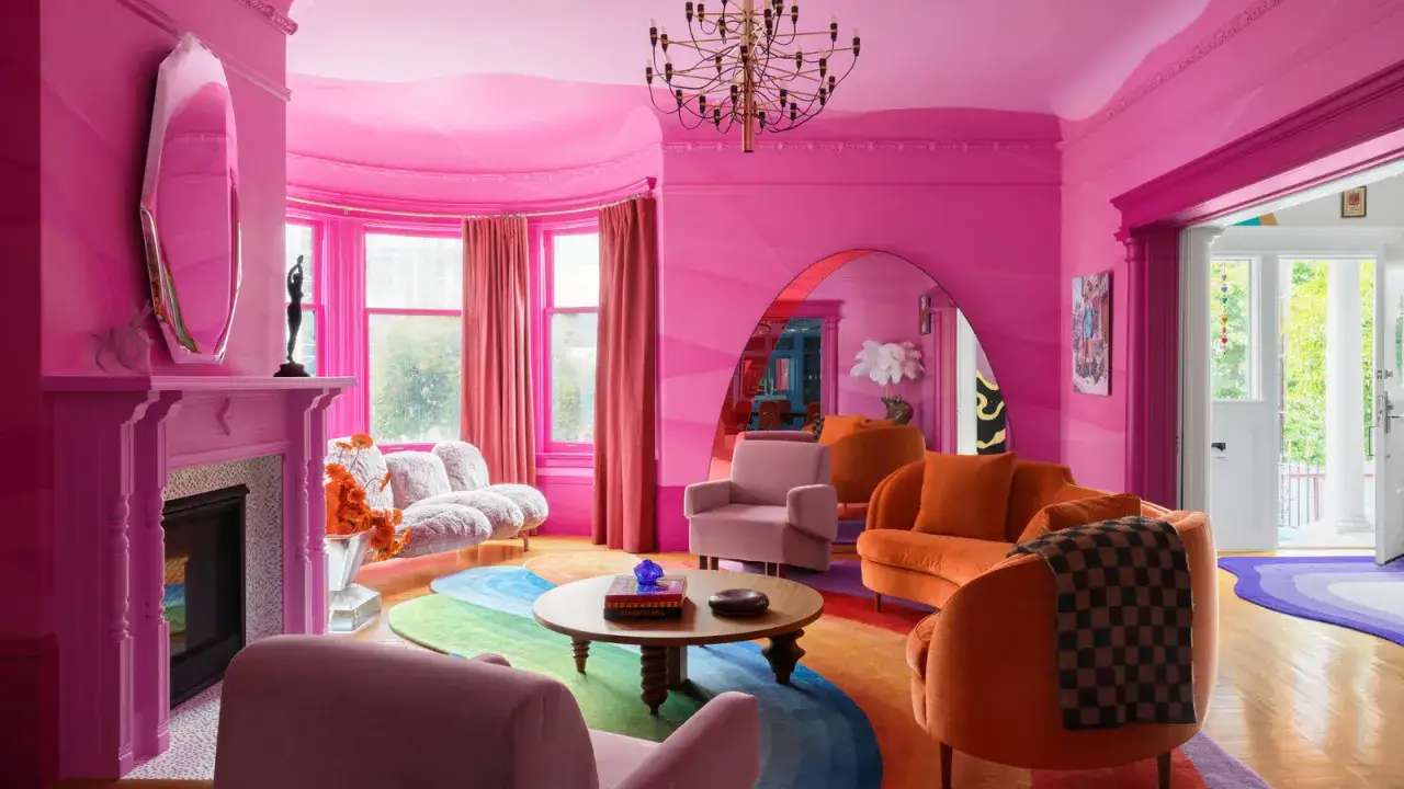 Salon rose vif avec des meubles orange vif et un tapis arc-en-ciel. Quelle couleur va avec le rose ? L'orange, le jaune, le bleu et le violet !