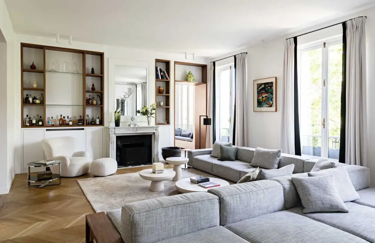 Salon moderne avec canapé gris, cheminée, étagères remplies de bouteilles et de verres. La décoration plafond salon est discrète, mettant en valeur l'espace.