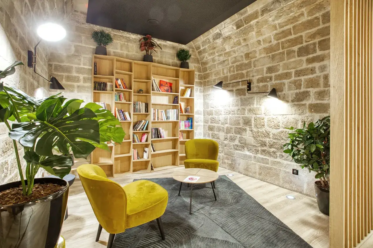 Un coin salon cosy avec deux fauteuils moutarde, une biblioth&egrave;que remplie de livres et des plantes vertes. Un espace de vie invitant &agrave; la d&eacute;tente.