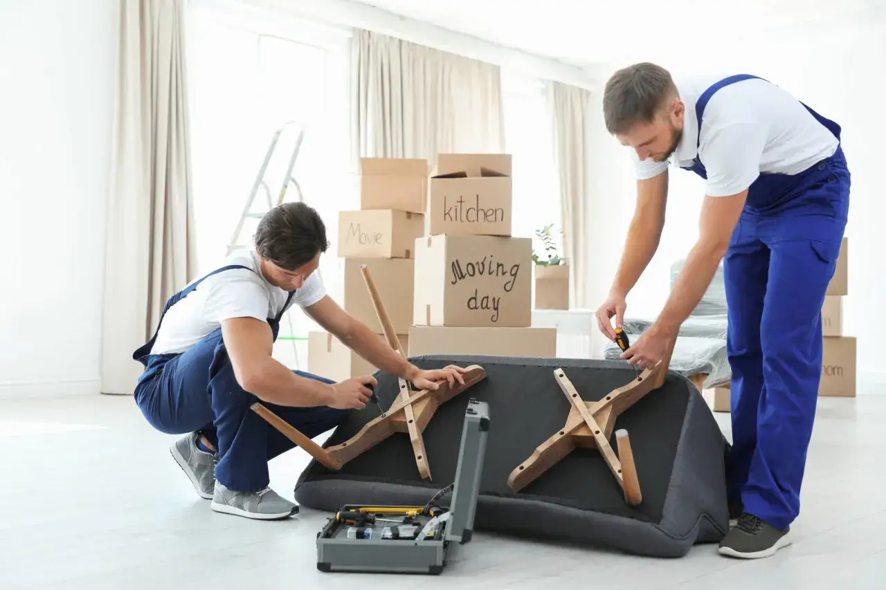 Deux d&eacute;m&eacute;nageurs s'occupent de comment d&eacute;monter un canap&eacute; fixe. Des cartons de d&eacute;m&eacute;nagement sont empil&eacute;s derri&egrave;re eux.