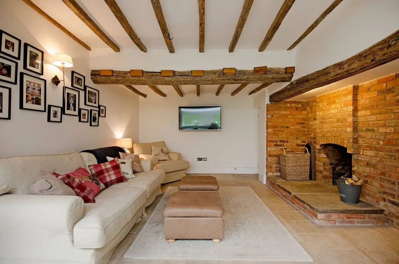Salon moderne avec poutre apparente. Un canapé confortable, une cheminée en briques et des poutres en bois au plafond créent une ambiance chaleureuse.