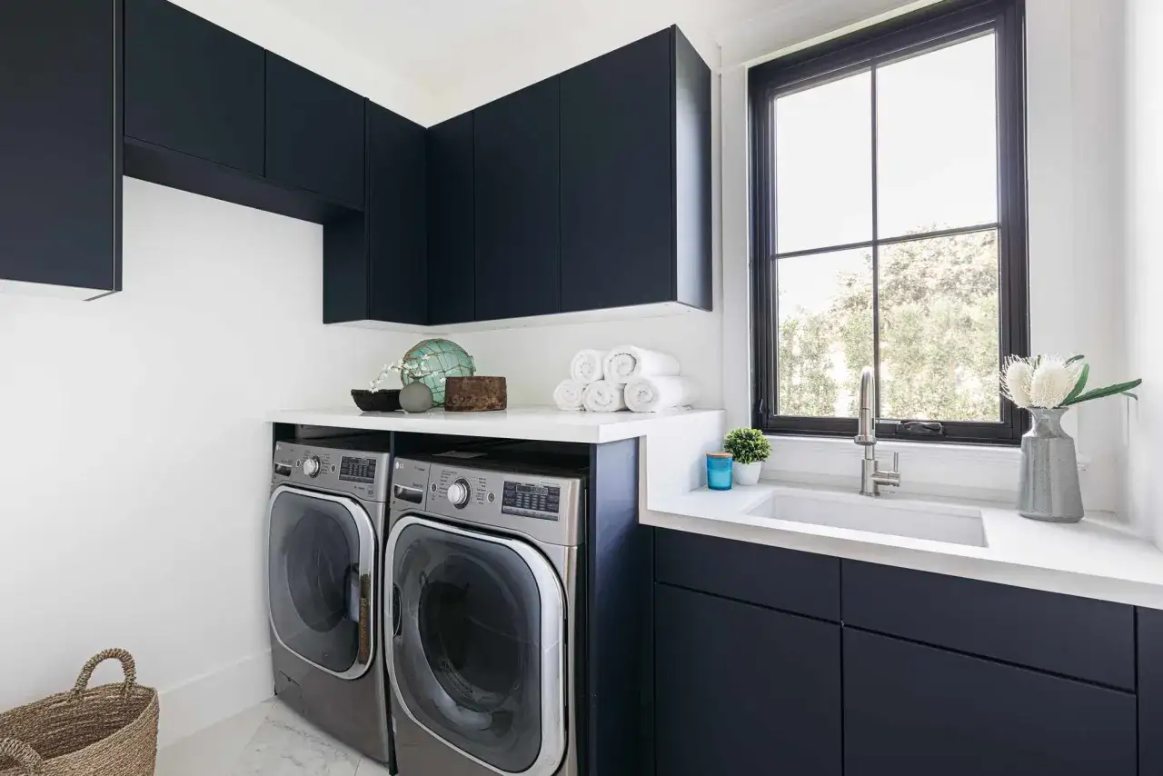 Linge propre et rangé dans cette buanderie moderne. La profondeur des meubles sombres met en valeur les machines à laver.