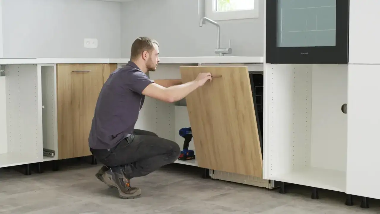 Un homme installe une porte de lave-vaisselle encastrable. Les dimensions sont importantes pour un bon ajustement.