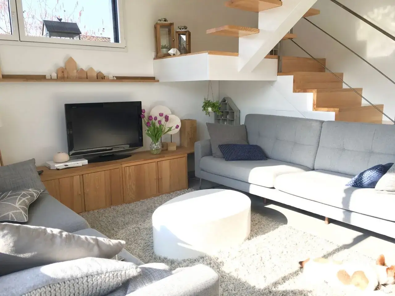 Un canapé gris confortable est installé sous un escalier en bois moderne, créant un coin salon cosy.