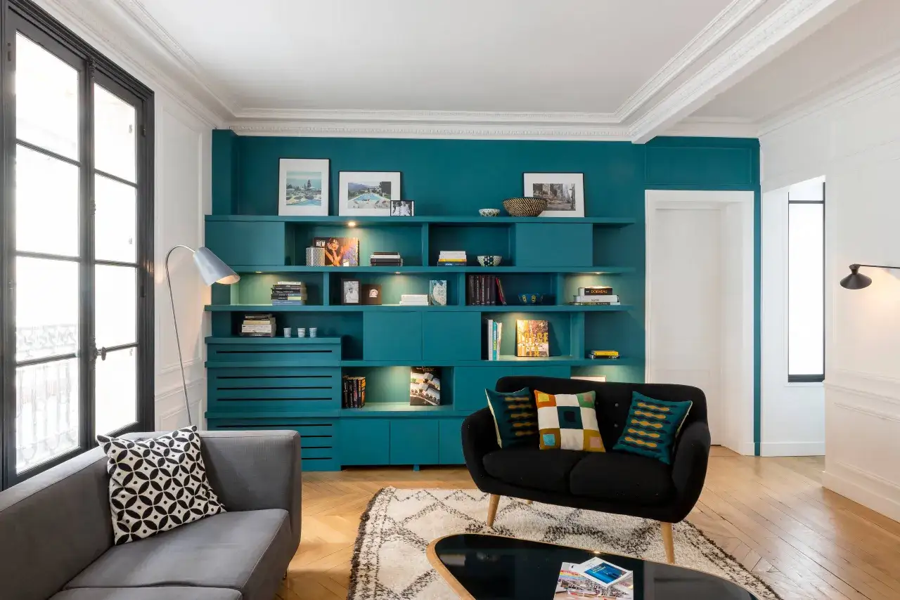 Comment &eacute;clairer une pi&egrave;ce sombre : un salon moderne avec une grande biblioth&egrave;que turquoise int&eacute;gr&eacute;e, des canap&eacute;s confortables et un &eacute;clairage subtil.